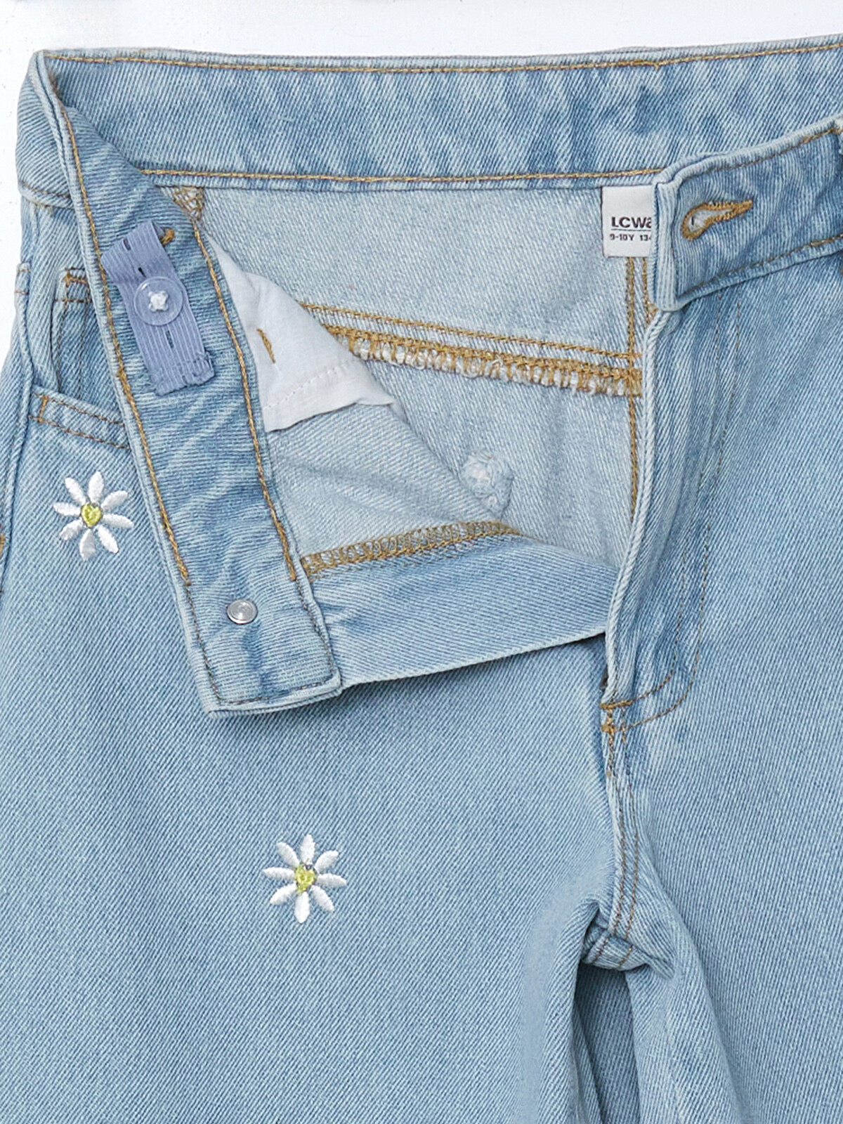 Close-up of embroidered daisies, denim waistband and button detail